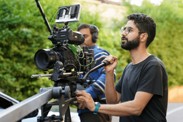 Cinematographer adjusting camera on green outdoor set.