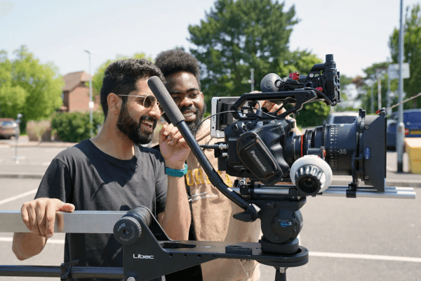 Cinematographer adjusting camera on tripod outdoors.